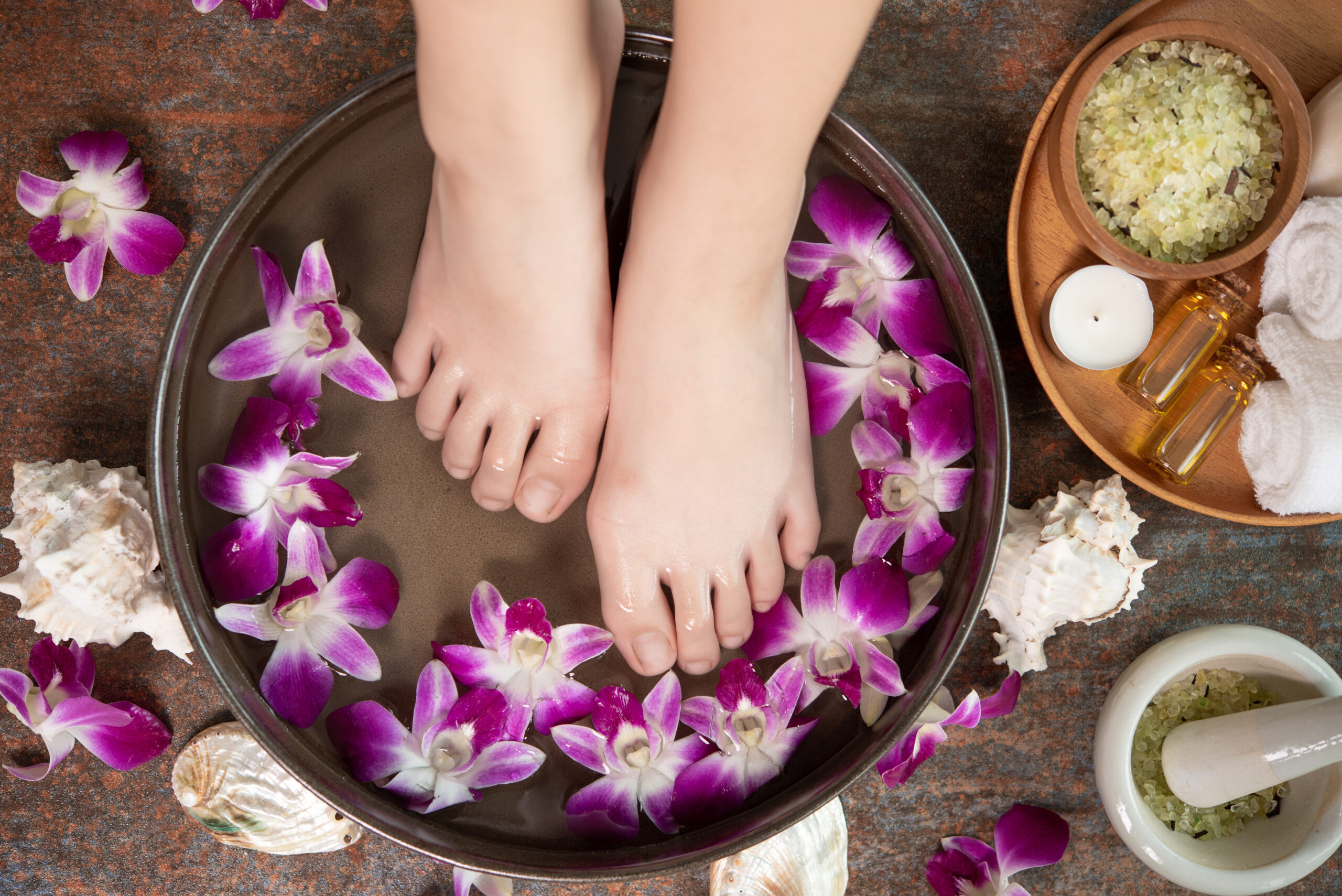 closeup view of woman soaking her hand and feet in dish with wat closeup view of woman soaking her hand and feet in dish with water and flowers on wooden floor. Spa treatment and product for female feet and hand spa. orchid flowers in ceramic bowl.
